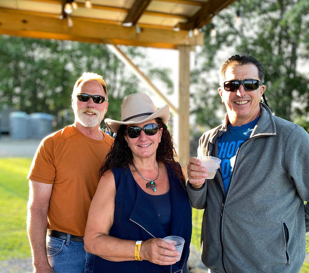 image of two men and 1 woman enjoying a wine tasting under the pergola at the concert venue